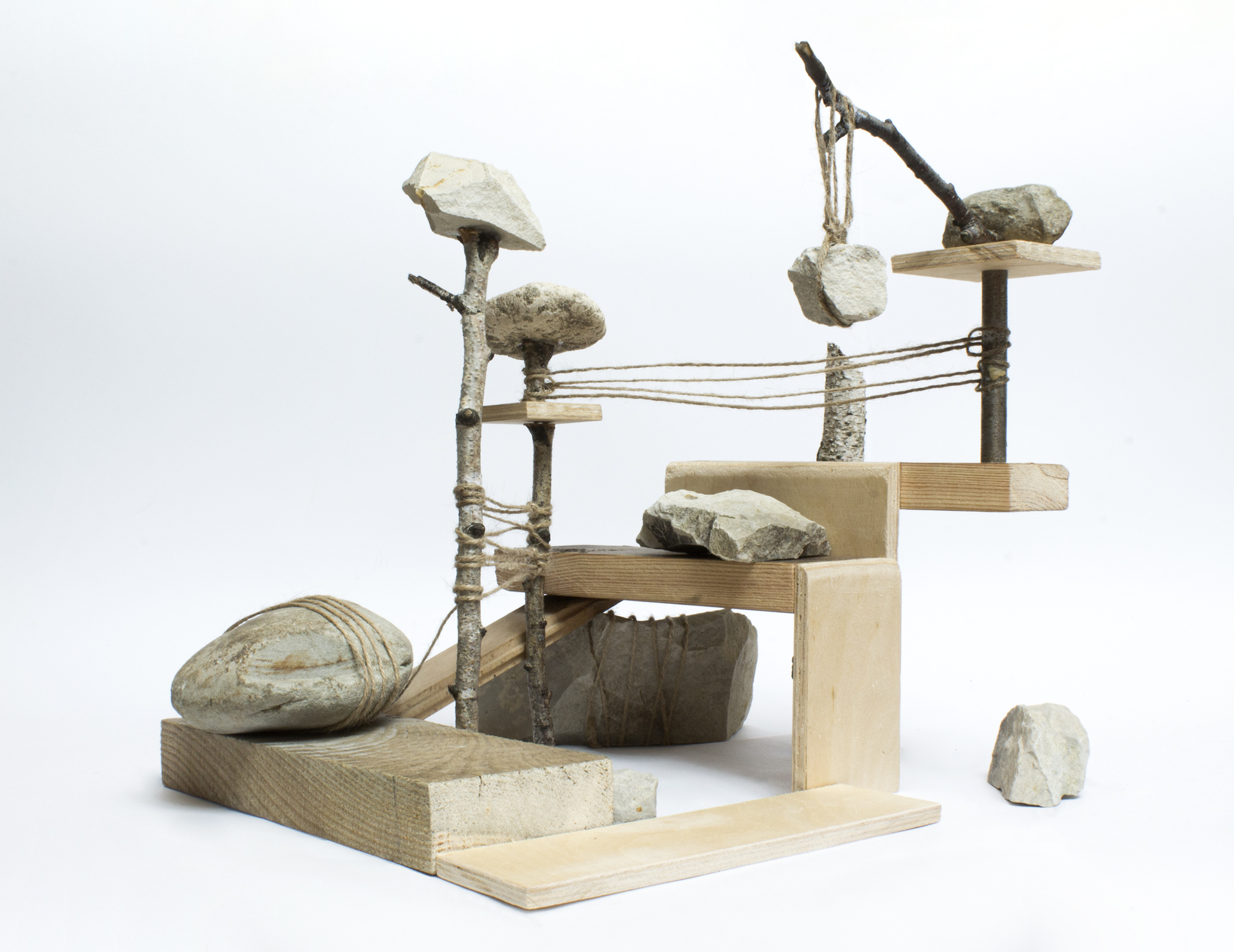 Abstrakcyjny, nieregularny układ z kamieni, sznurków i drewna umieszczony na jasnoszarym  tle.