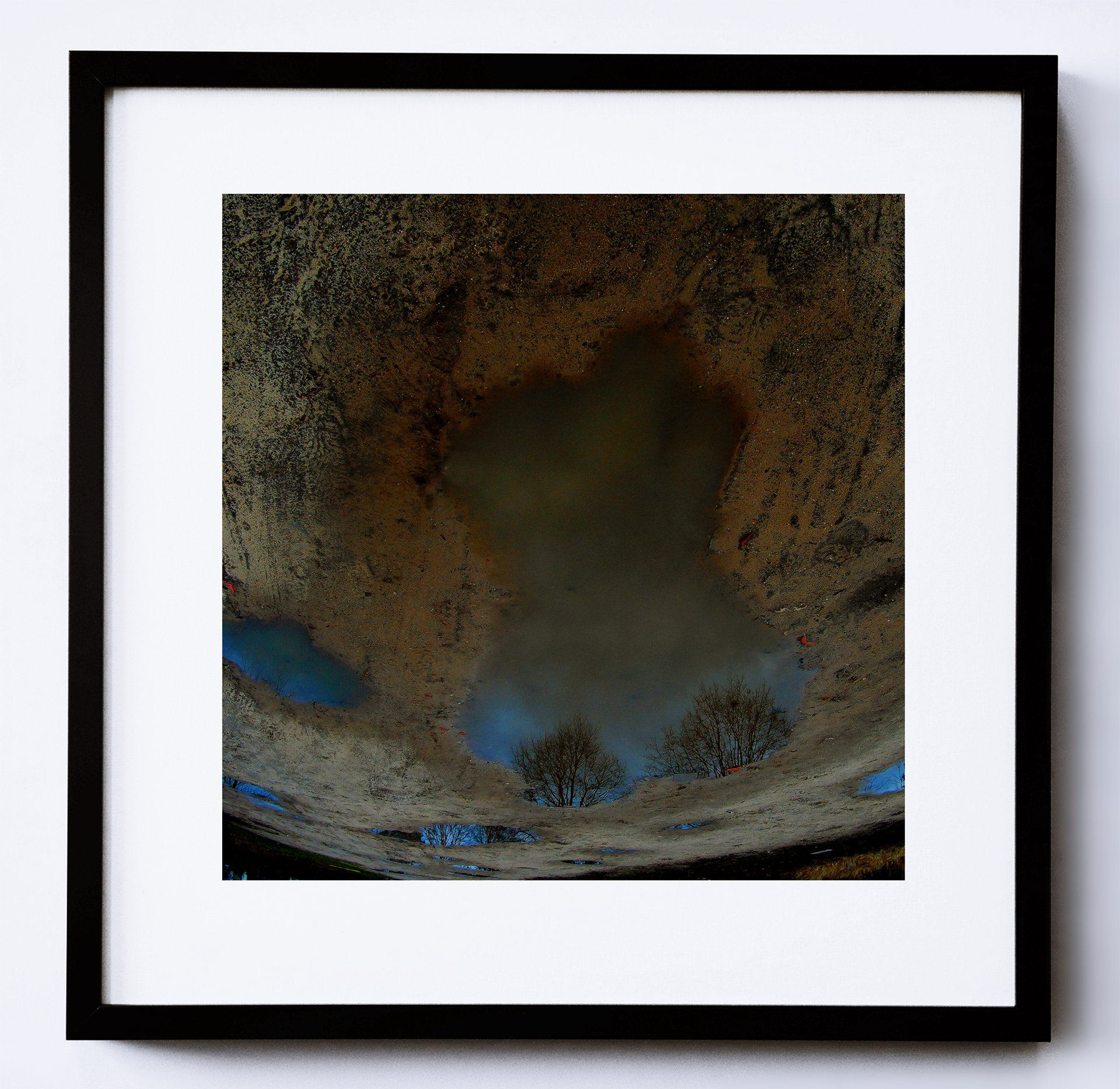 Kolorowa fotografia, utrzymana w ciemnej kolorystyce, ukazująca kałużę z odbijającymi się w niej fragmentami nieba.