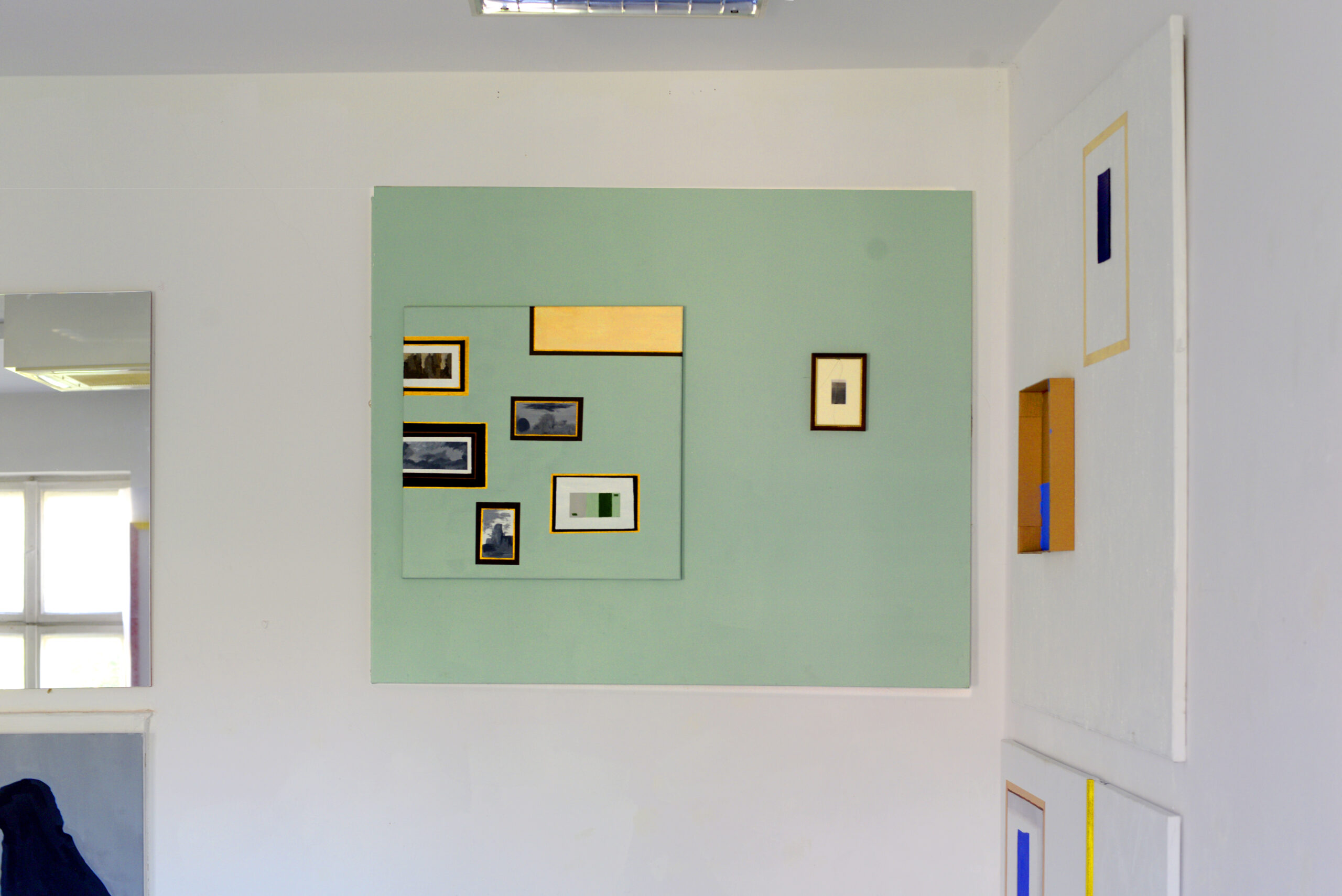 Obraz przedstawia zieloną ścianę z zawieszonymi na niej oprawionymi fotografiami.