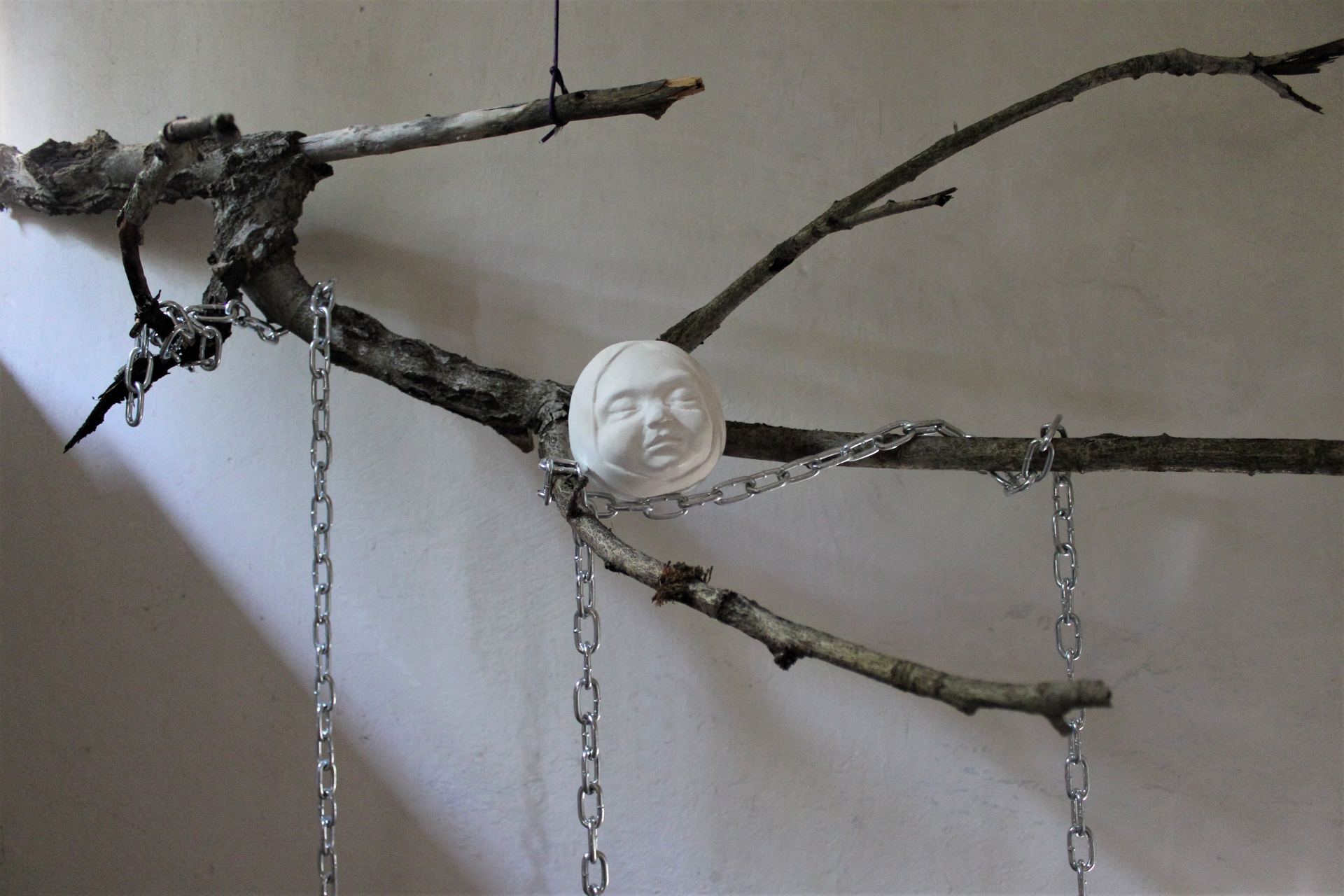 Instalacja składająca się z gałęzi i łańcuchów na której zawieszone są białerzeźby dziecięcych głów, których forma może kojarzyć się z jabłkiem