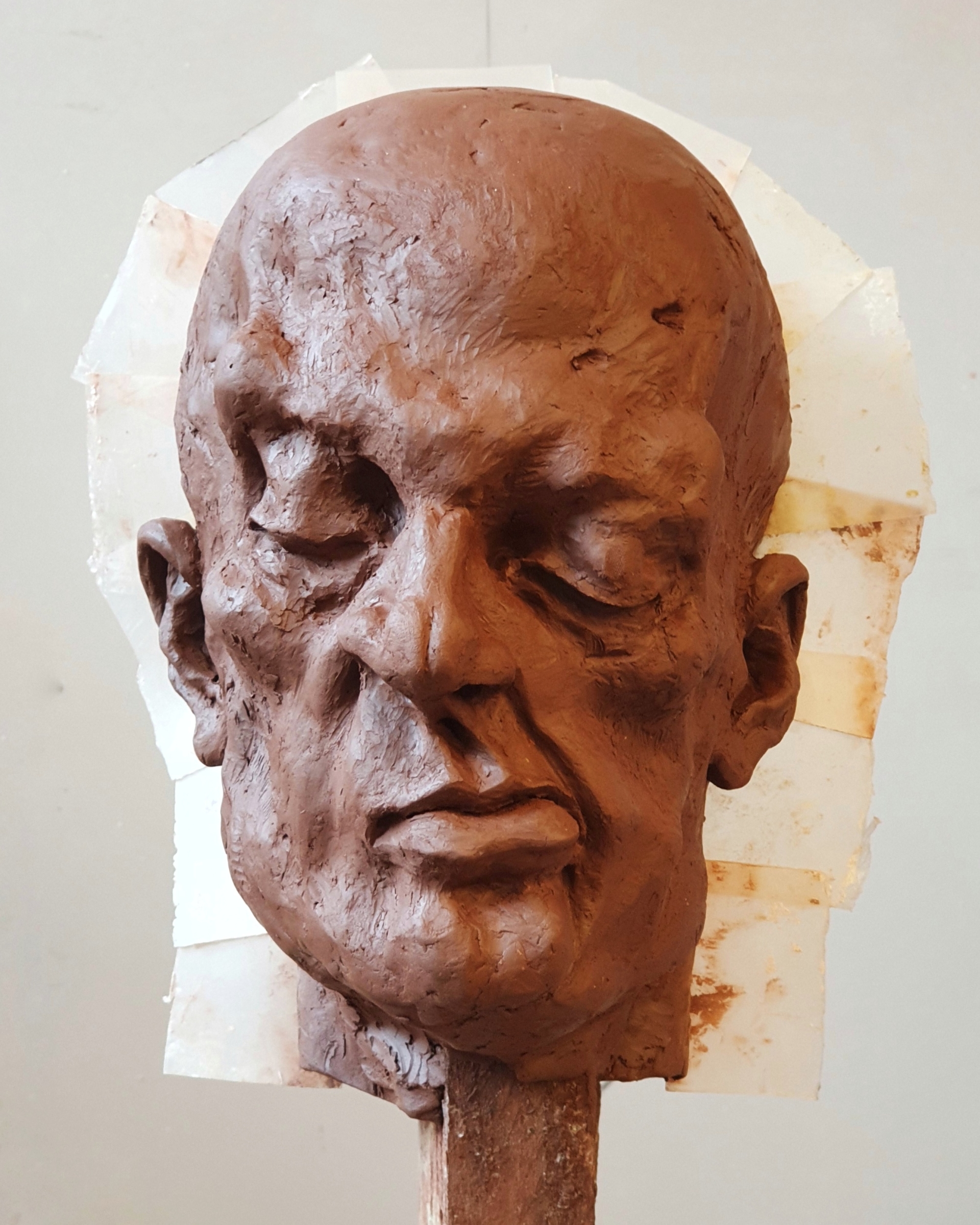 Portret gliniany przedstawiający łysą, groteskową postać o skrzywionej wgrymasie twarzy i zmrużonych oczach.