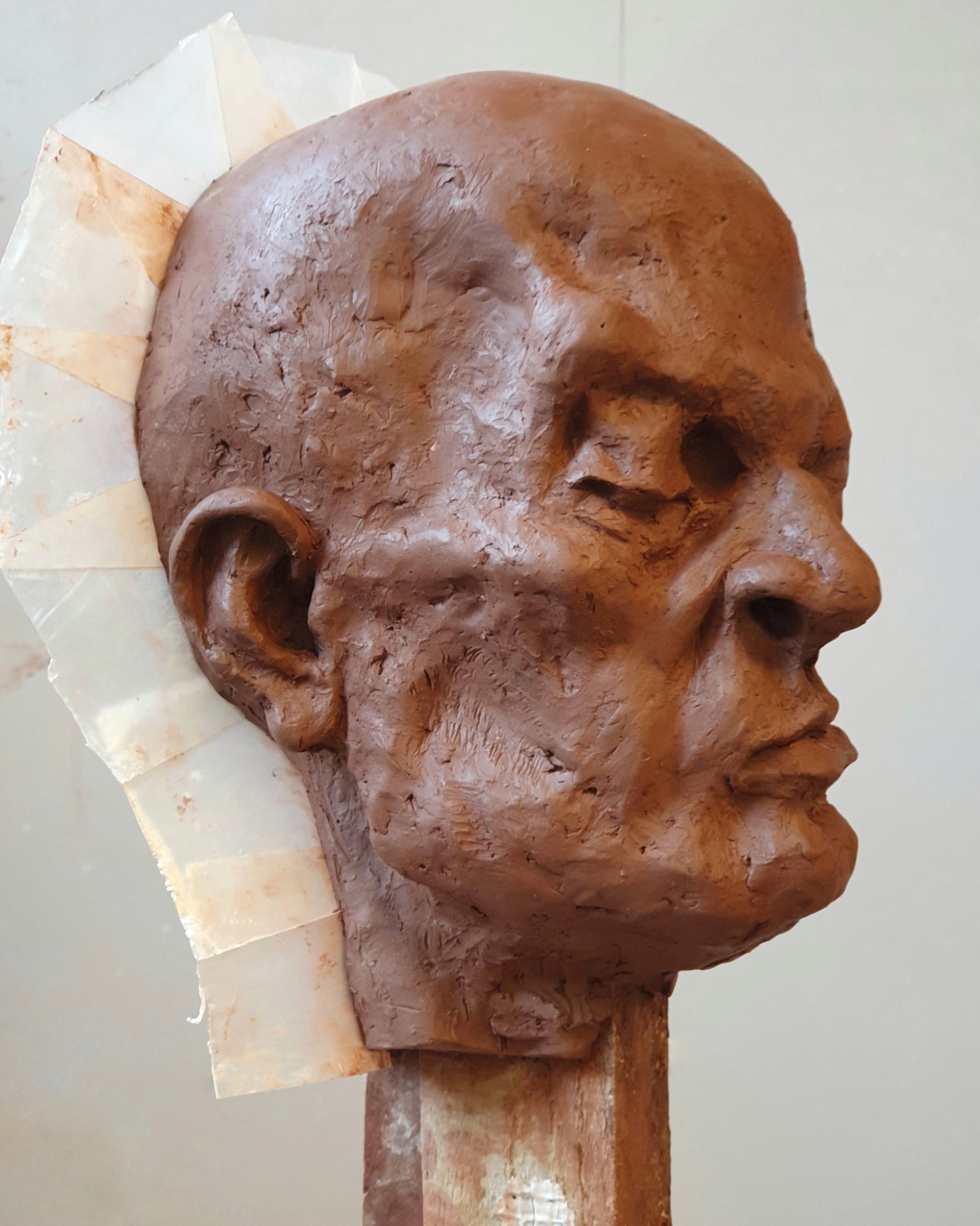 Portret gliniany przedstawiający łysą, groteskową postać o skrzywionej wgrymasie twarzy i zmrużonych oczach.