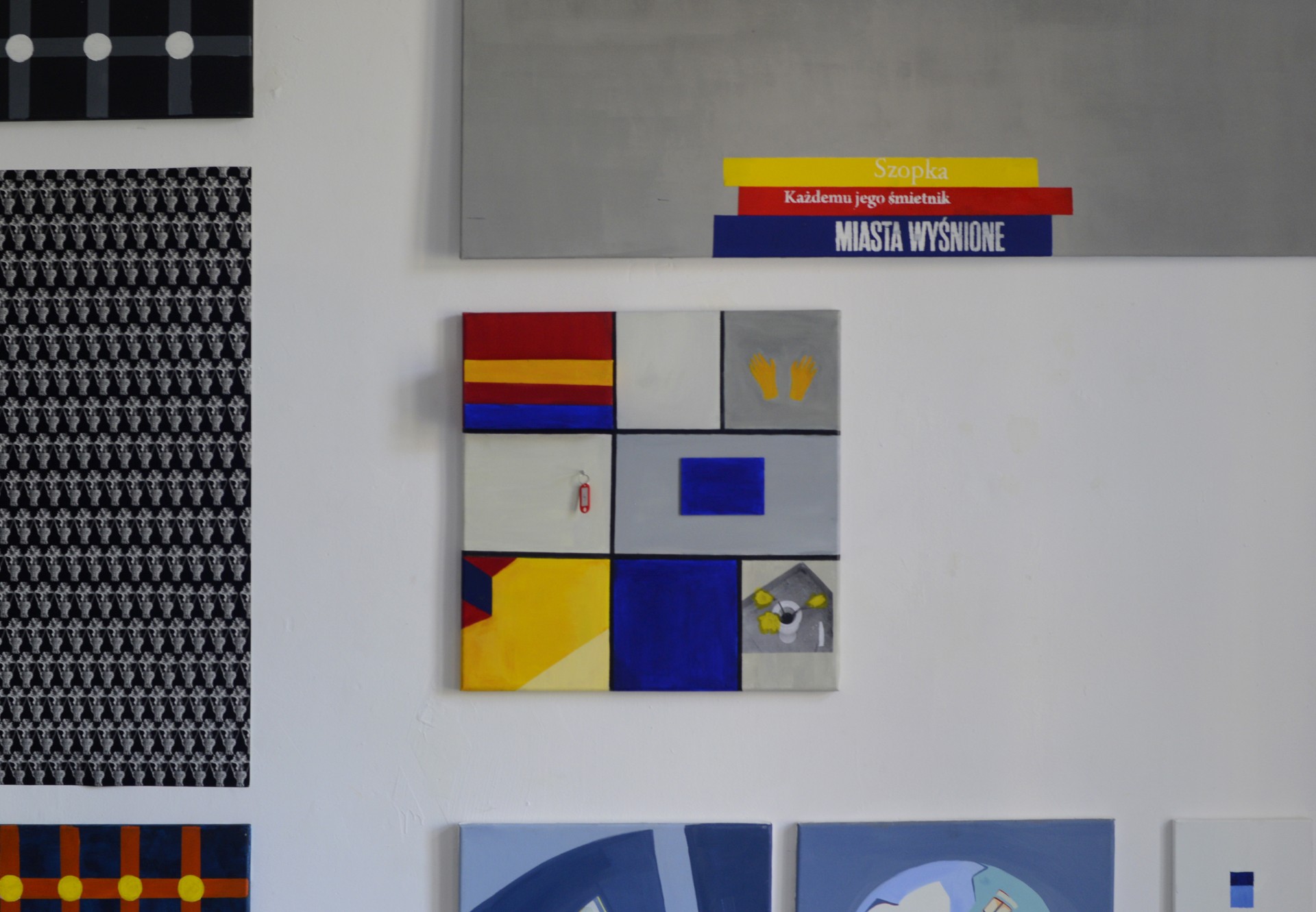Zdjęcie przedstawia ścianę w pracowni. W centrum zawieszony został obraz w trzech kolorach podstawowych z zawieszonym na nim kluczu i kolorowym pudełkiem.