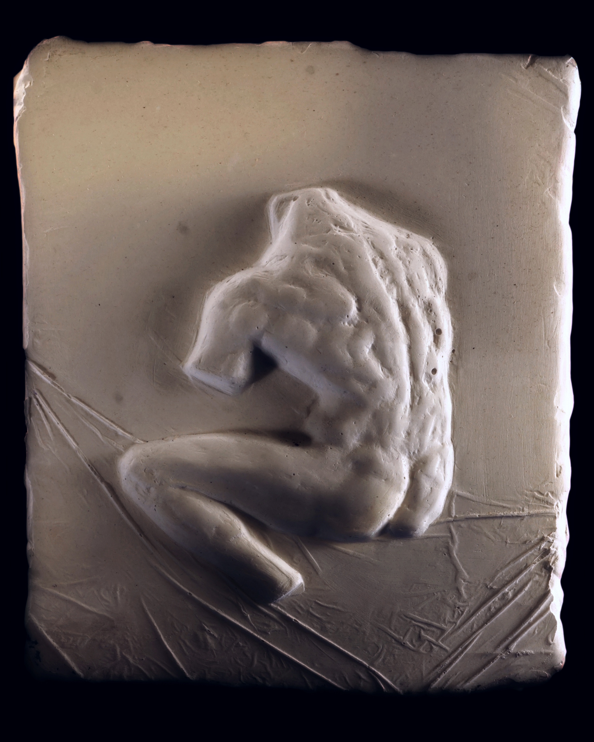 J.Osika - zdjęcie przedstawia płaskorzeźbę ukazująca męski akt zwrócony do widza plecami, bez kończyn i głowy, wykonano w gipsie.