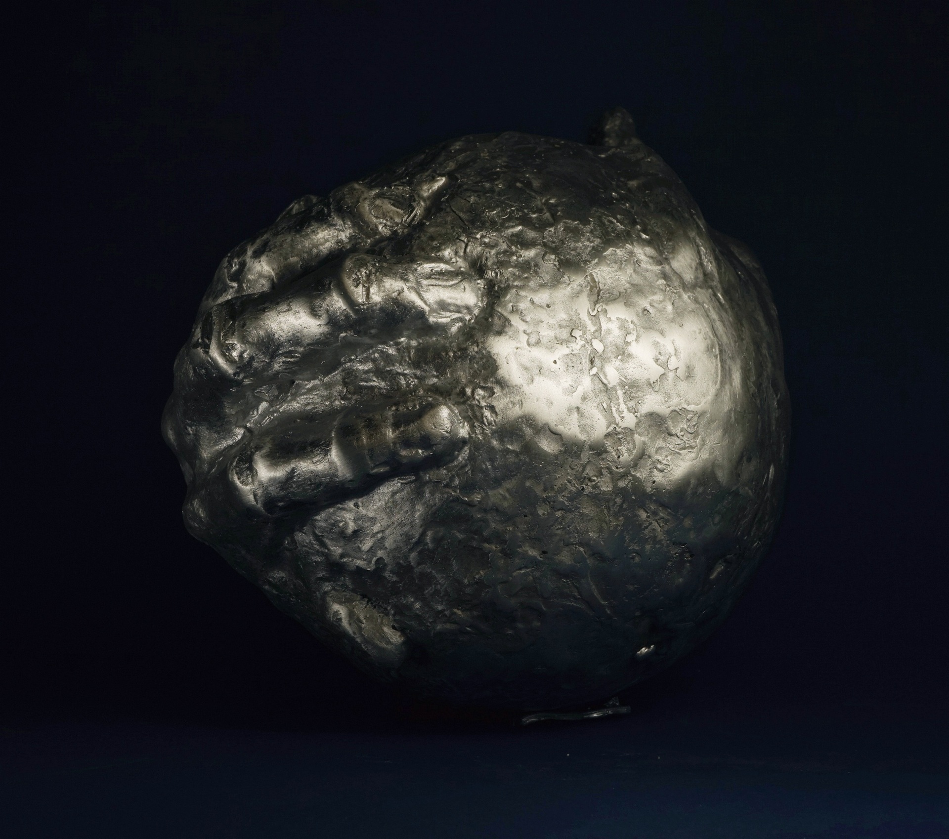 Anna Mandziak - zdjęcie przedstawiające rzeźbę kuli obejmowaną dłońmi, wykonaną z aluminium.