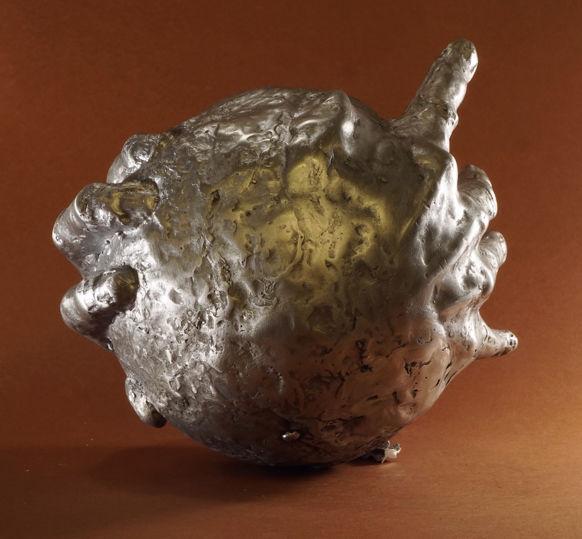 Anna Mandziak - zdjęcie przedstawiające rzeźbę kuli obejmowaną dłońmi, wykonaną z aluminium. 