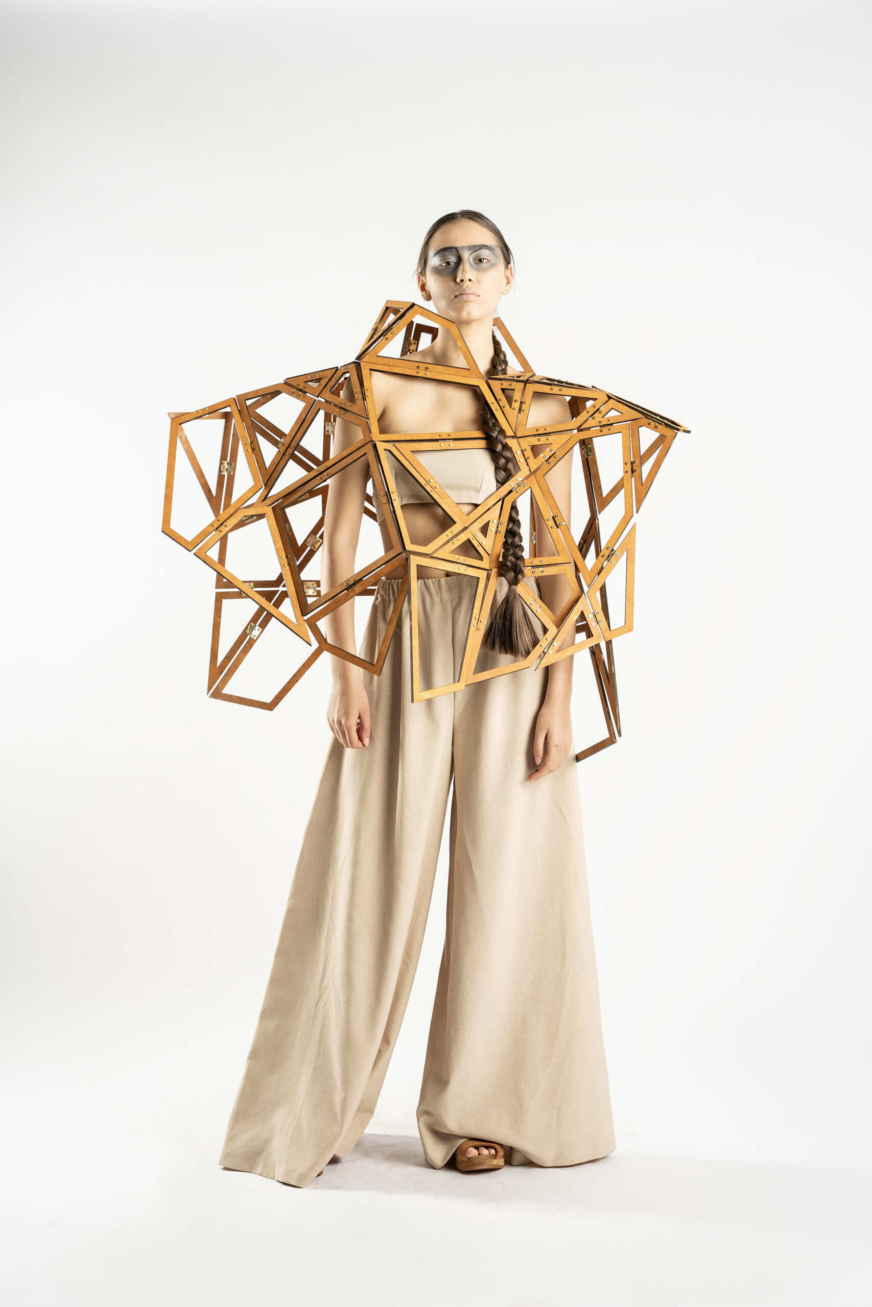 Zdjęcie kobiety w spodniach, topie i drewnianej, geometrycznej, ażurowej konstrukcji na ramionach