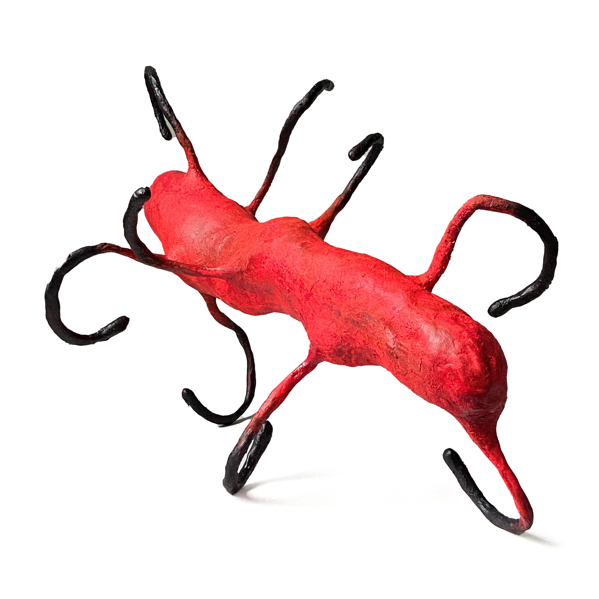 Czerwony, podłużny, organiczny obiekt rzeźbiarski z dziewięcioma podwiniętymi czarnymi odnóżami. Przypomina owada.