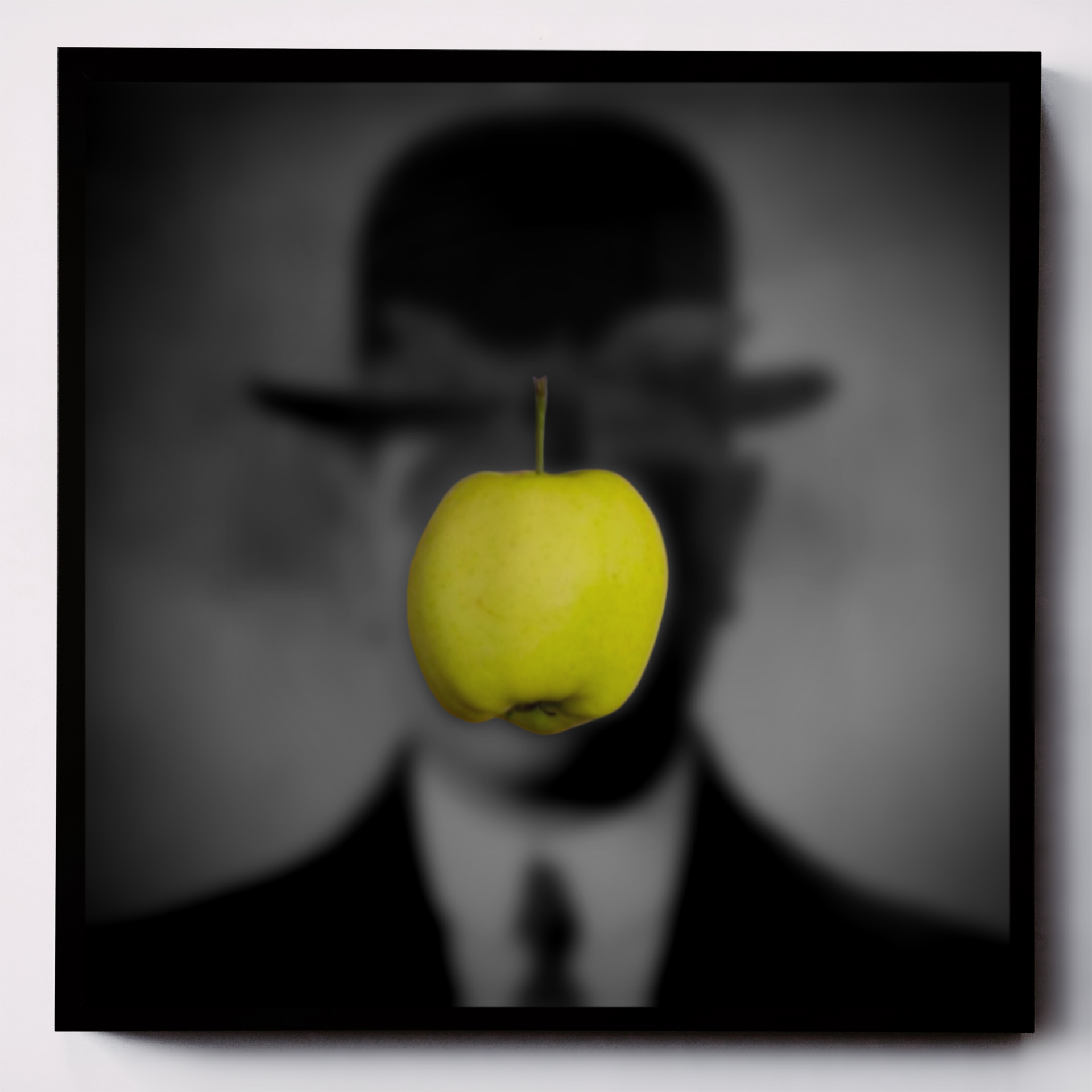 Kompozycja graficzna przedstawiająca zielone jabłko na tle nieostrego czarno-białego tła ukazującego niewyraźny portret mężczyzny w meloniku.   	