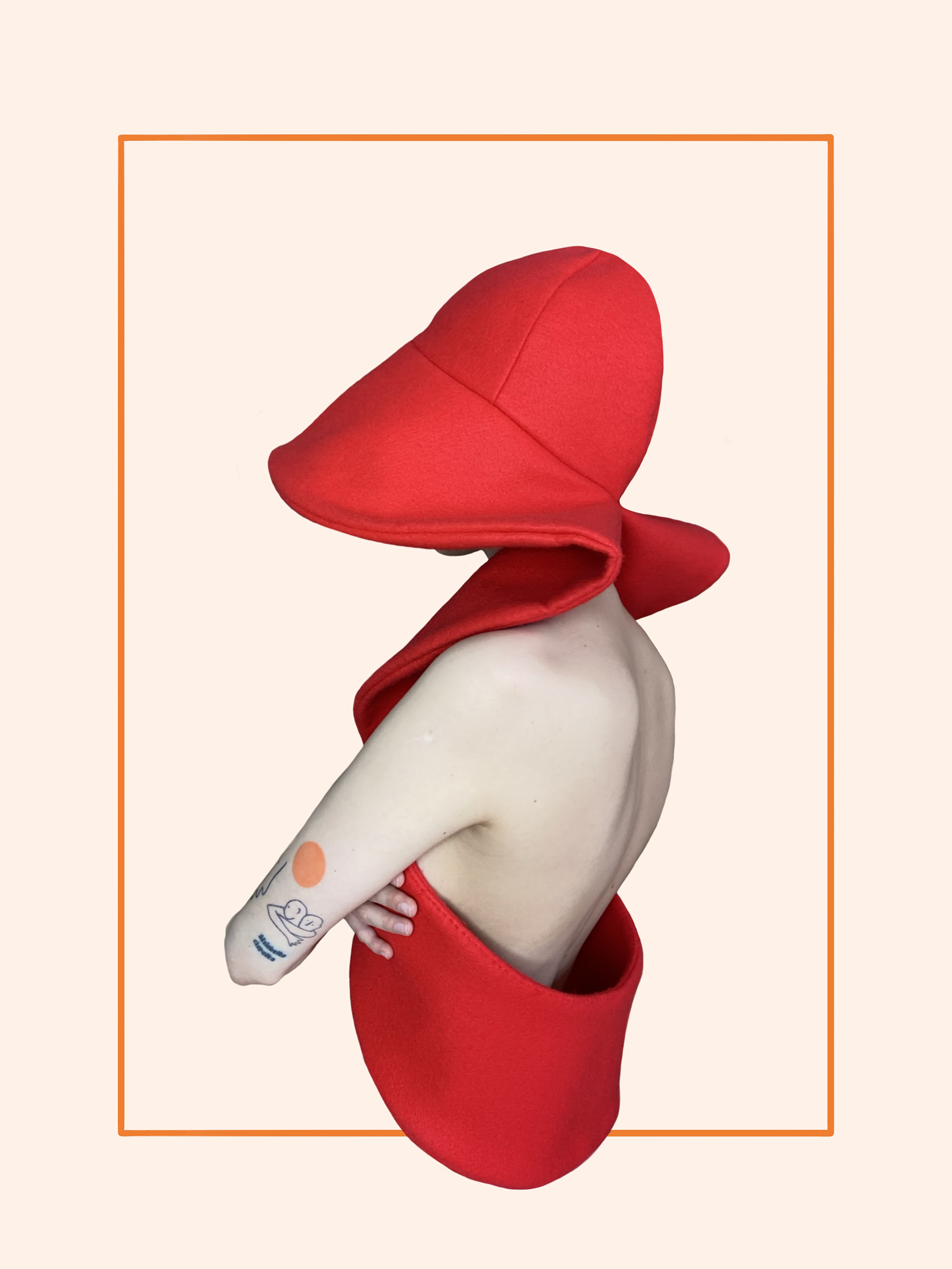 Osoba widoczna od pasa w górę pod skosem od tyłu. Ubrana w czerwoną sztywną formę kapelusza połączonego z kamizelką. Widoczne nagie plecy i ramię. Tło neutralne beżowe.