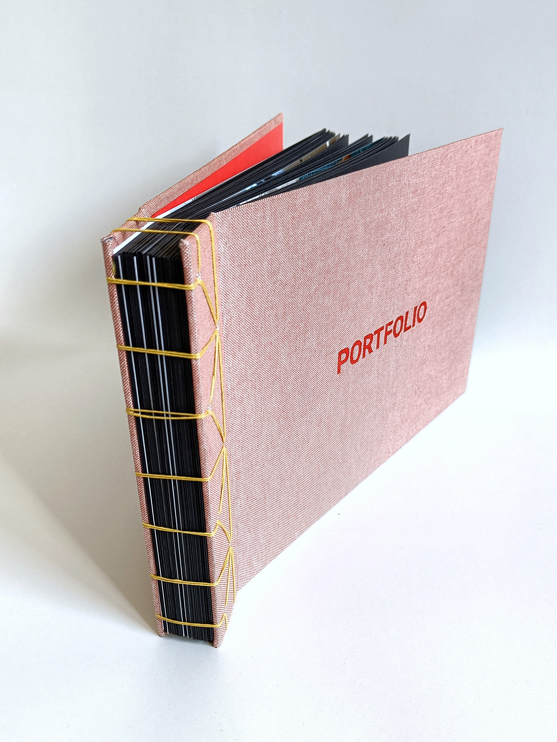 Fotografia przedstawia Portfolio w formie albumu, z widocznym szyciem żółtą nitką na grzbiecie, oprawa sztywna, na okładce widoczny tłoczony napis PORTFOLIO.