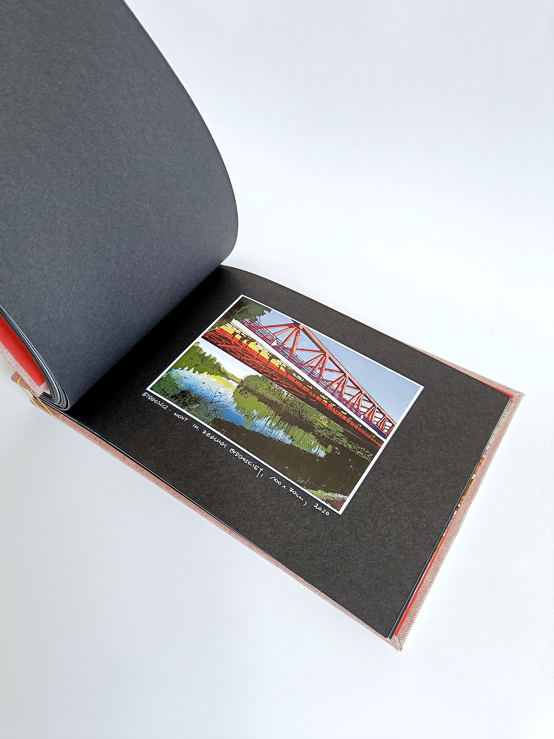 Fotografia przedstawia otwarte Portfolio w formie albumu, na czarnych kartkach widoczna grafika przedstawiająca stary metalowy most.