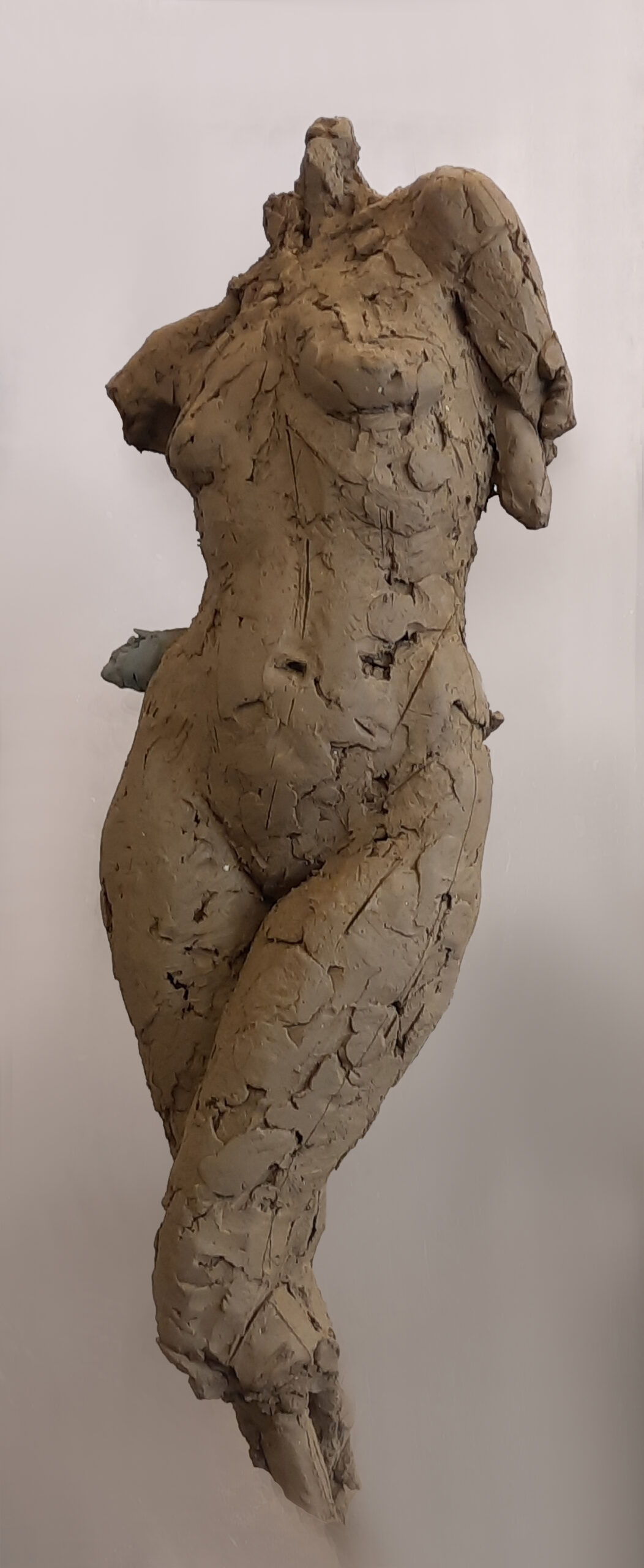 zdjęcie przedstawia rzeźbę z gliny- postać kobiecą w ujęciu od szyi do kolan, bez rąk,  jedna noga lekko ugięta. Struktura rzeźby fakturalna,ujęcie frontalne