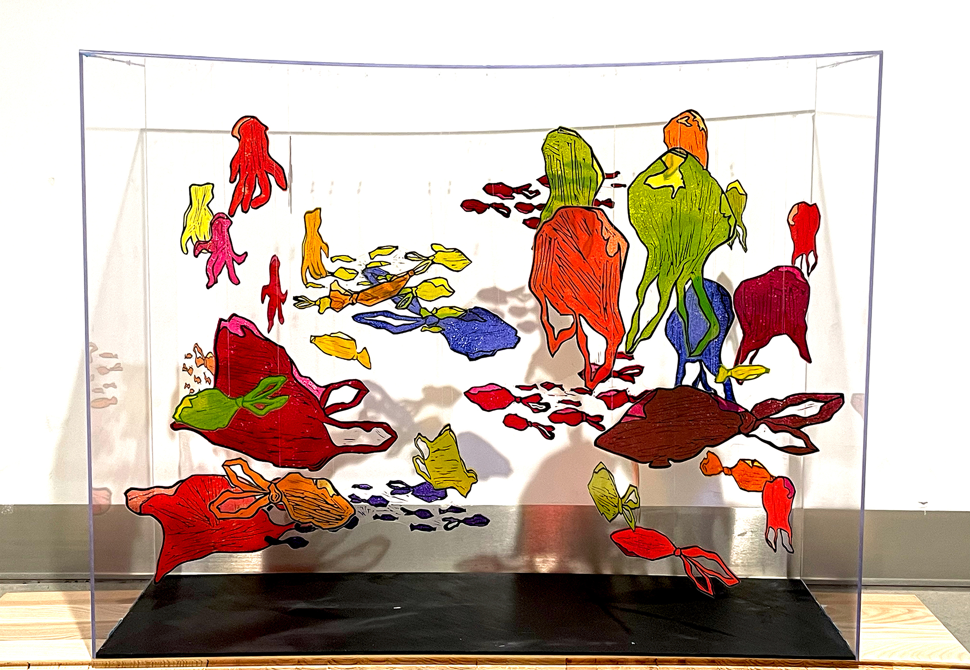 Fotografia przedstawia obiekt w formie akwarium wypełnionego wykonaną linorytem ławicą kolorowych reklamówek w kształtach przypominających ryby