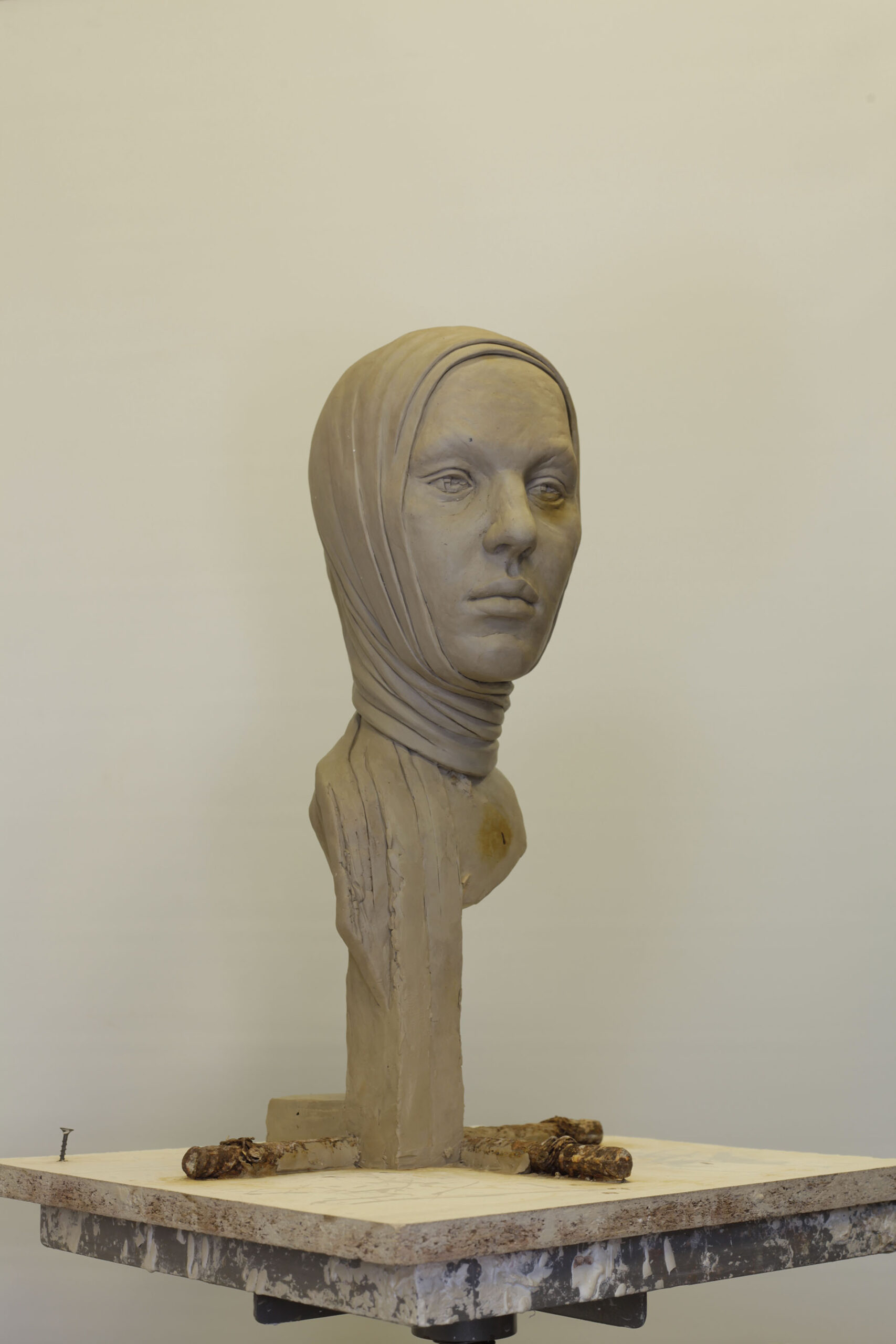 Zdjęcie przedstawia rzeźbę portretową o neutralnym wyrazie twarzy, wokół głowy i szyi znajduje się charakterystyczna forma w kształcie chusty.