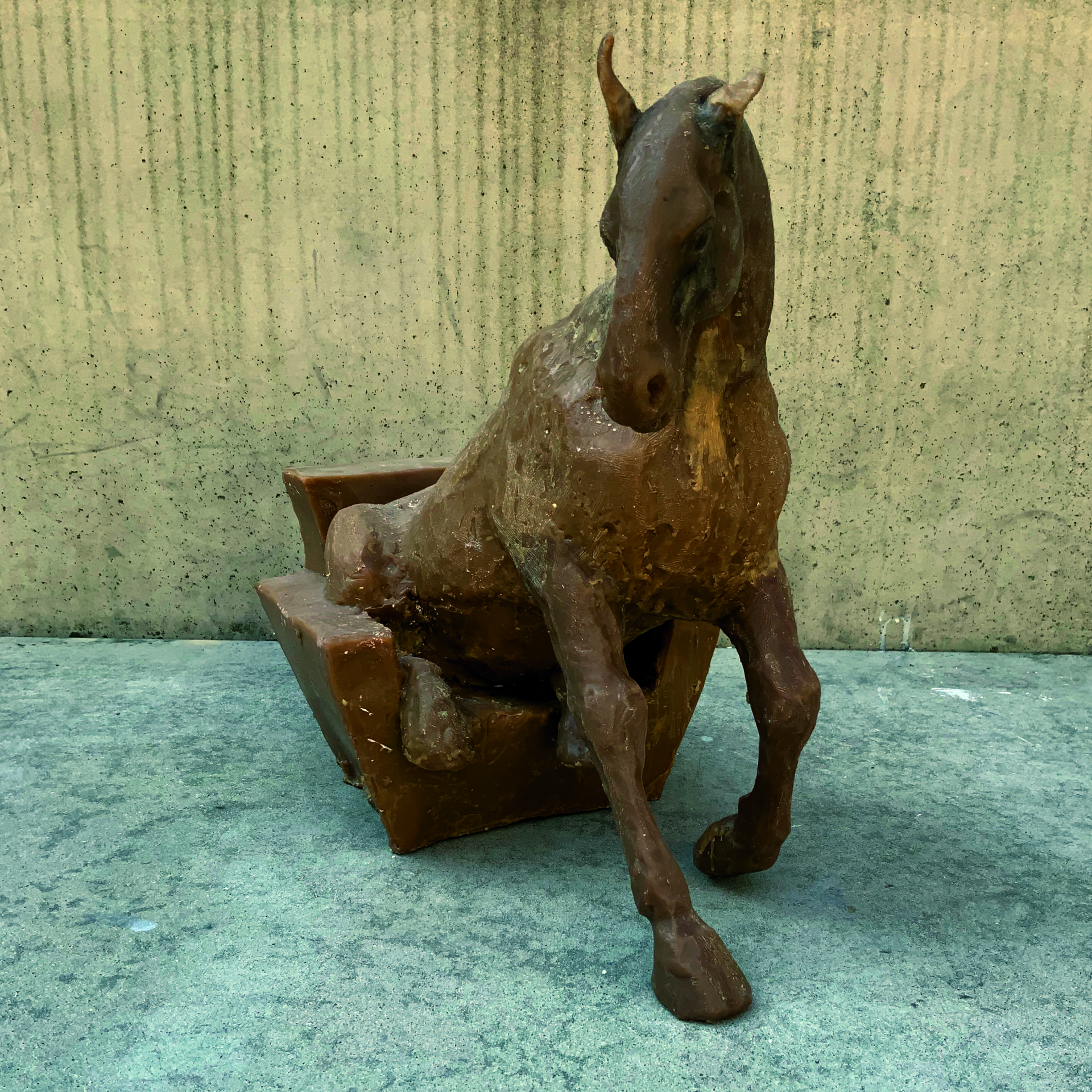 Woskowa rzeźba przedstawiająca konia próbującego usiąść na fotelu.