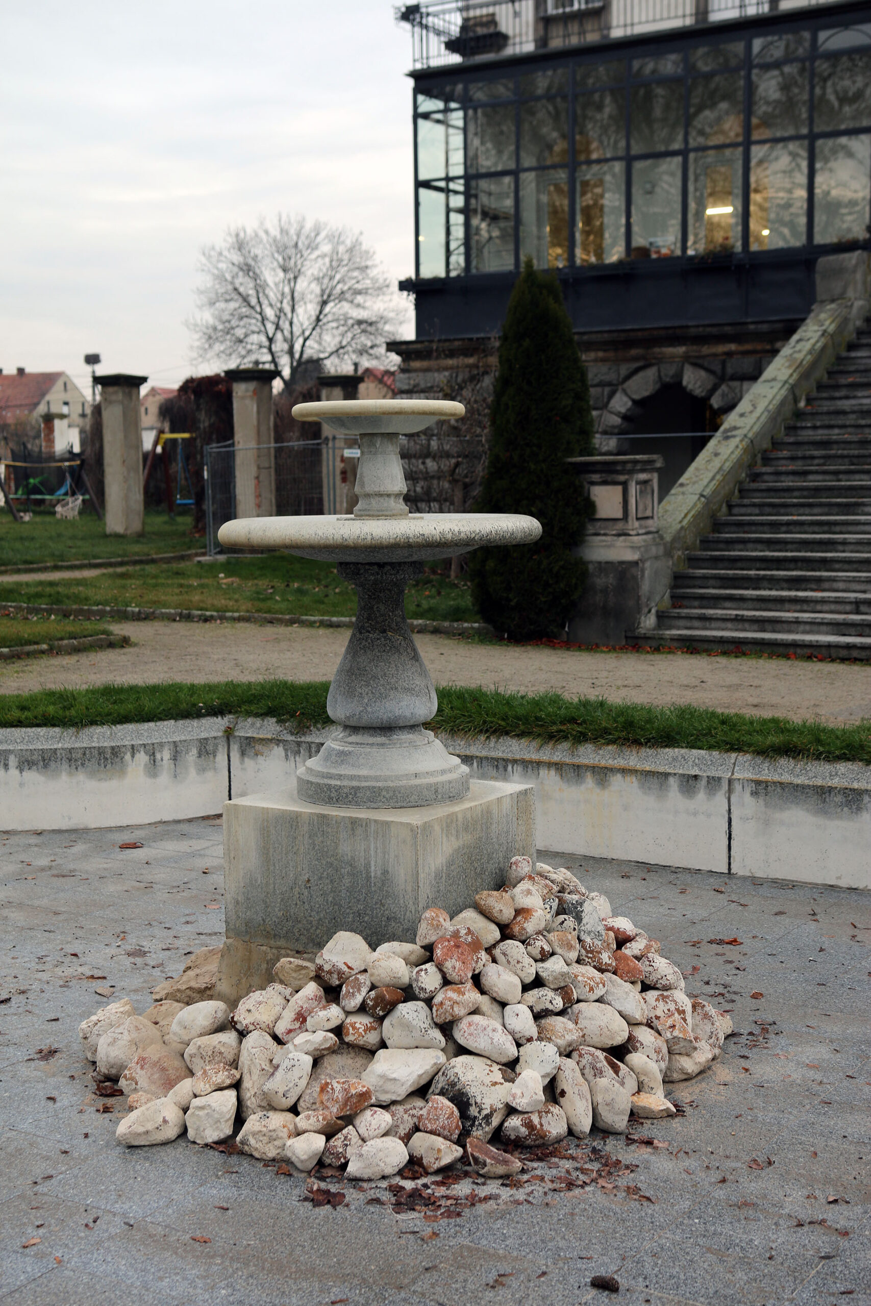 Zdjęcie przedstawia suchą kamienną fontannę, której cokół został obłożony stosem białych kamieni