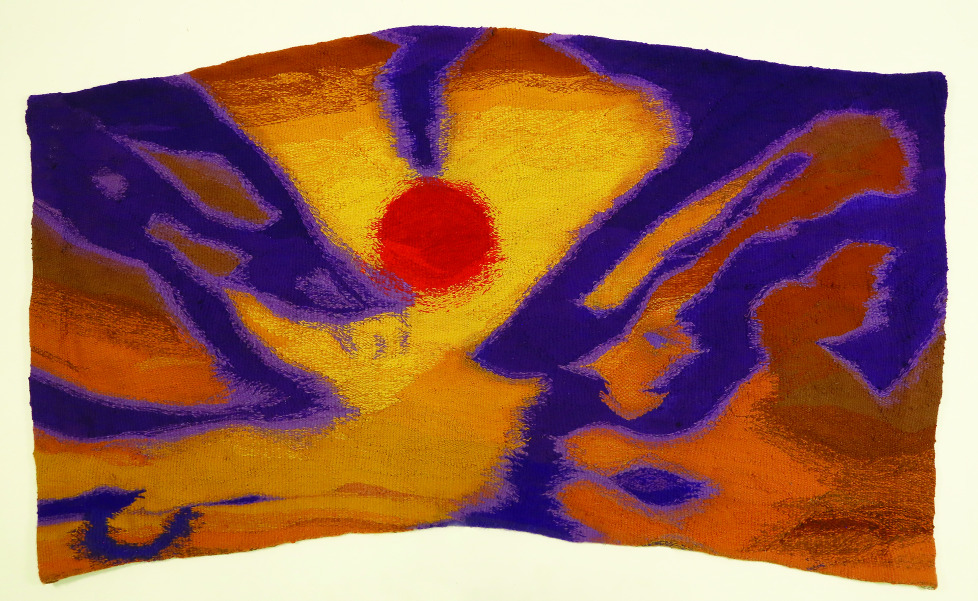  Zdjęcie przedstawia tkaninę w nieregularnym formacie. Górna i dolna krawędź jest wygięta w łuk. W centrum tkaniny znajduje się czerwony owalny kształt, otoczony abstrakcyjnymi formami koloru fioletowego na pomarańczowym tle.