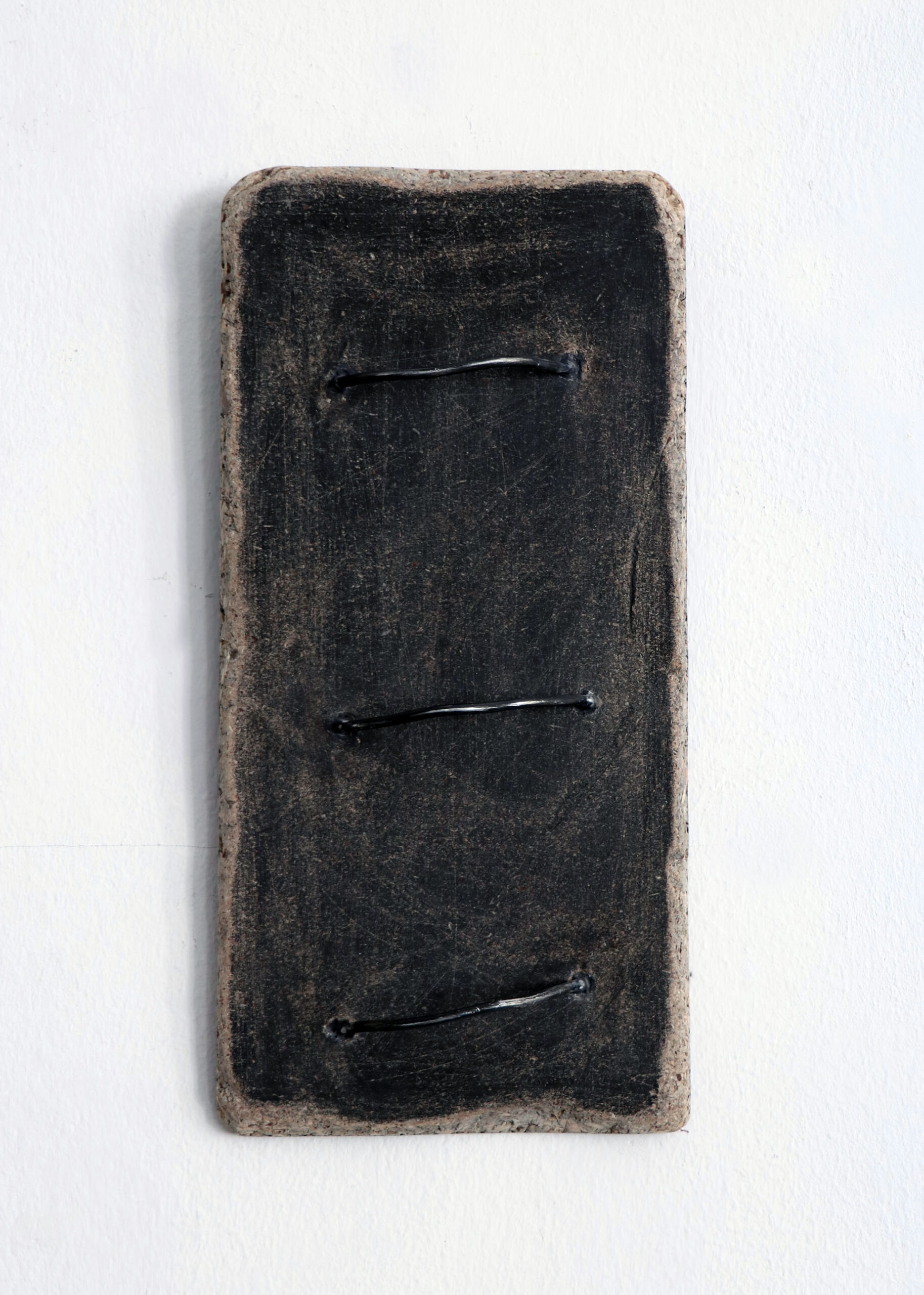 Zdjęcie przedstawia ciemną drewnianą, prostokątną płytkę z wystającymi metalowymi elementami
