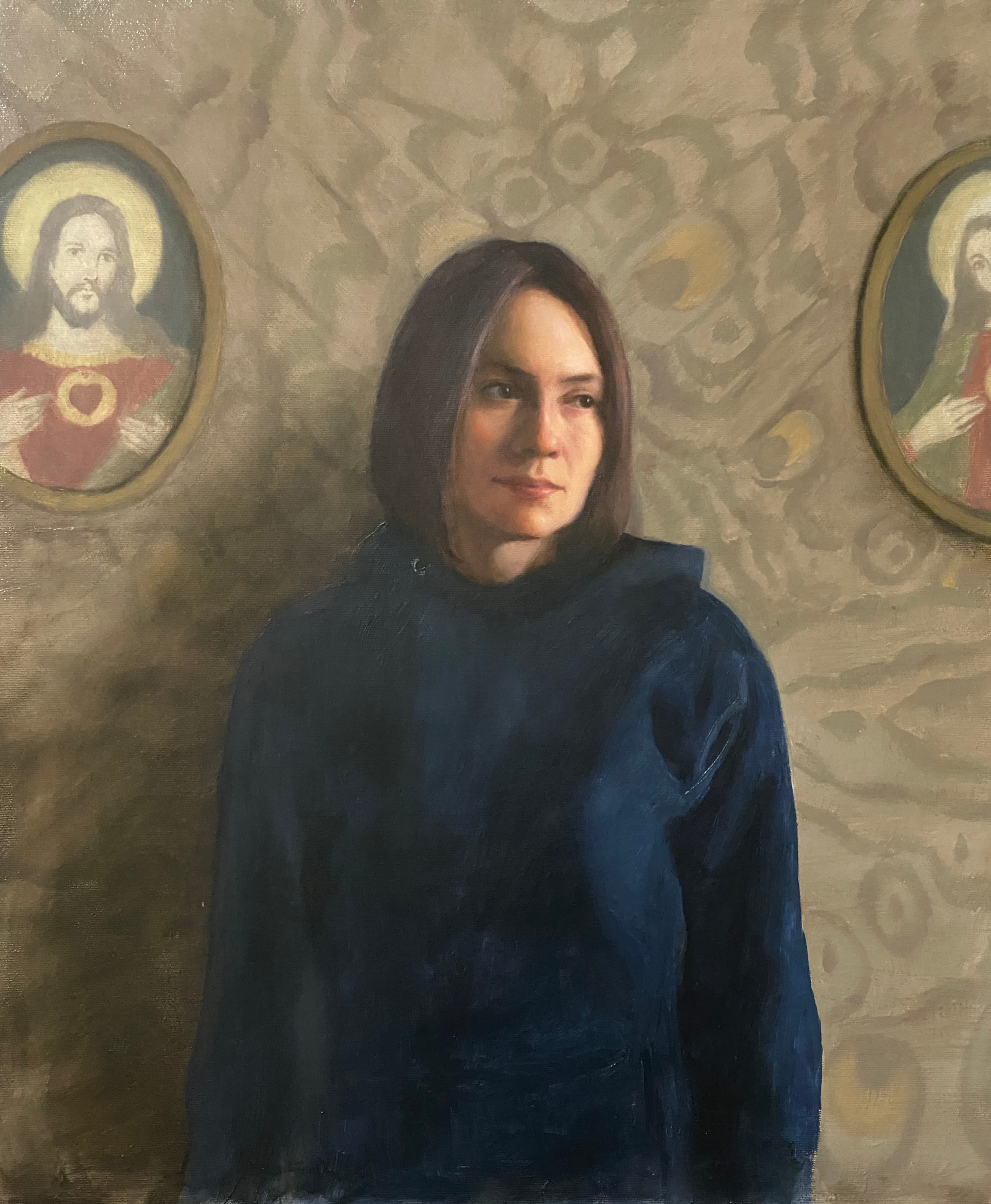 Obraz stojącej postaci kobiecej na tle ściany z tapetą. Po bokach obrazy o tematyce religijnej.