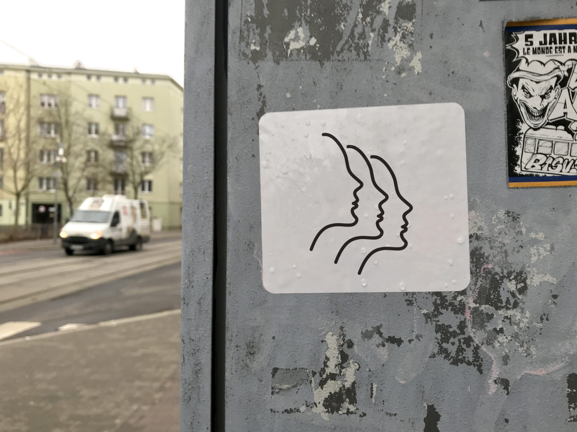Naklejka przyklejona w przestrzeni miejskiej/ulica przedstawiająca schematyczny rysunek trzech damskich profili.