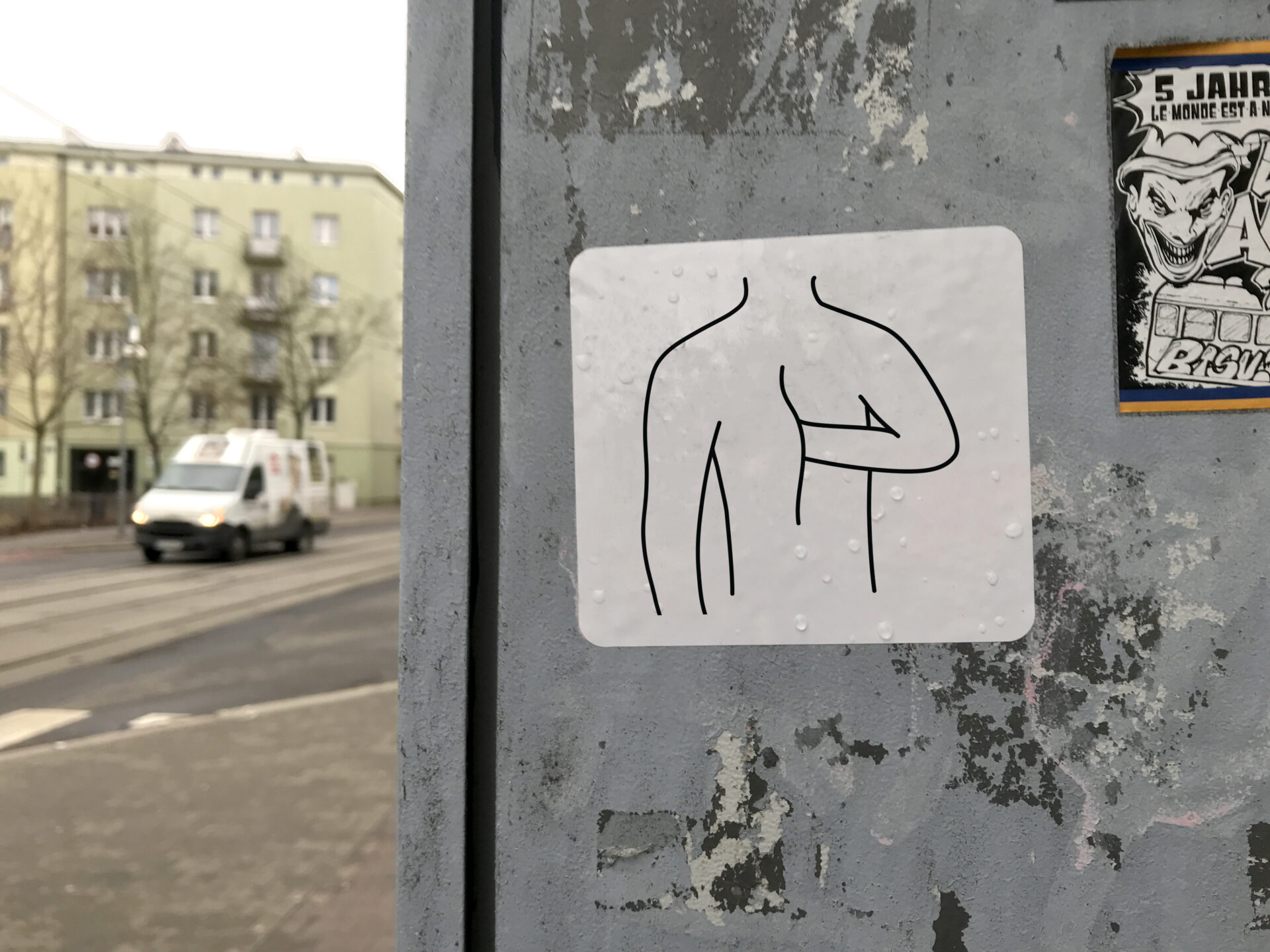 Naklejka przyklejona w przestrzeni miejskiej/ulica przedstawiająca schematyczny rysunek ludzkiego torsu bez głowy, jedna ręka wnika w ciało w okolicy brzucha.